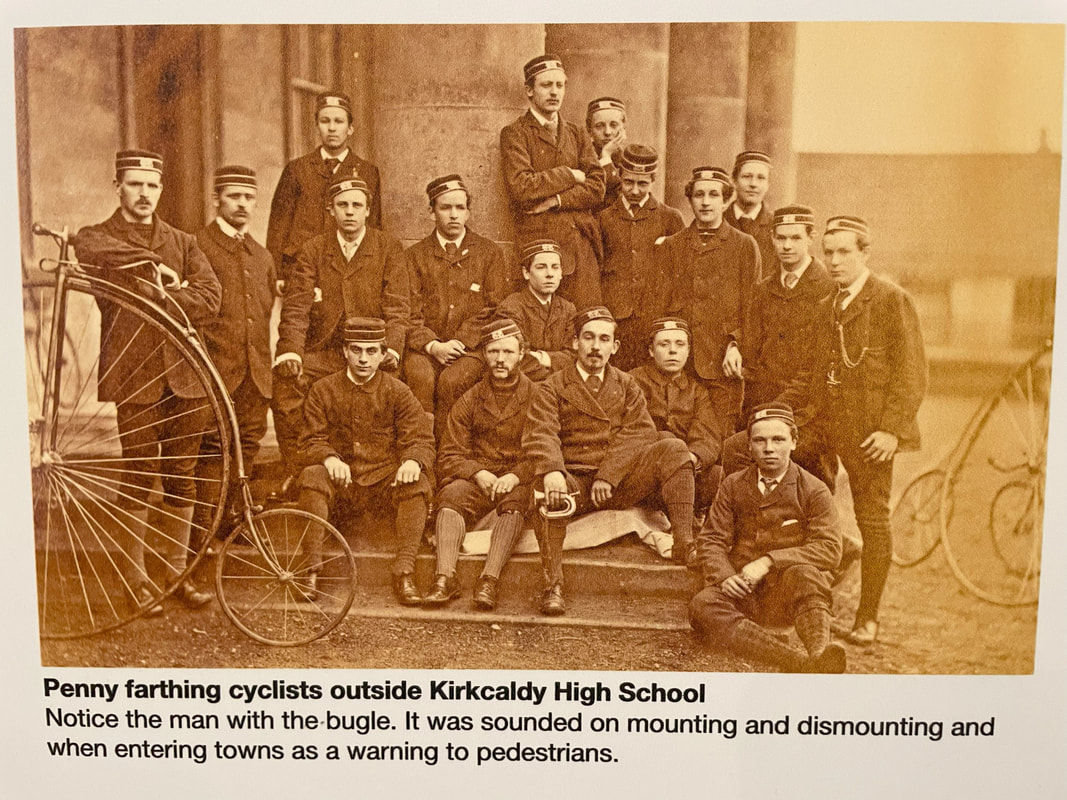 Photo of Penny farthing cyclists in Kirkcaldy. The photo is in Kirkcaldy galleries. They are all men and wear uniforms with caps. One of the men holds a bugle